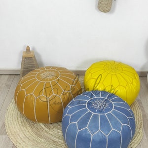 May include: Three poufs, one yellow, one brown, and one blue, with white stitching and a star design. The poufs are on a woven straw mat.