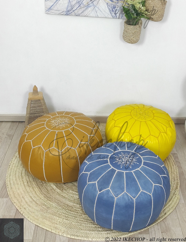 May include: Three poufs, one yellow, one brown, and one blue, with white stitching and a star design. The poufs are on a woven straw mat.