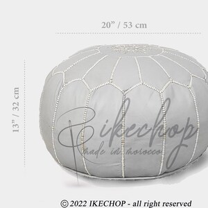 May include: A gray leather pouf with white stitching, measuring 20 inches in diameter and 13 inches in height. The pouf has a traditional Moroccan design with a hexagonal pattern.