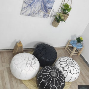 May include: Four poufs, two black and two white, with intricate stitching and a star design in the center. The poufs are arranged on a woven rug.