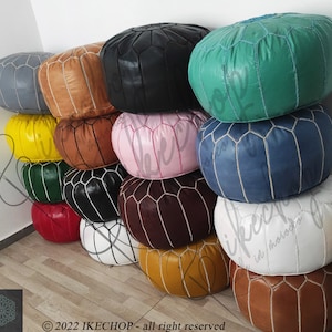 May include: A stack of colorful poufs made of leather with white stitching. The poufs are arranged in a pyramid shape, with the largest pouf at the bottom and the smallest pouf at the top. The poufs are in various colors, including yellow, green, blue, red, brown, black, and white.