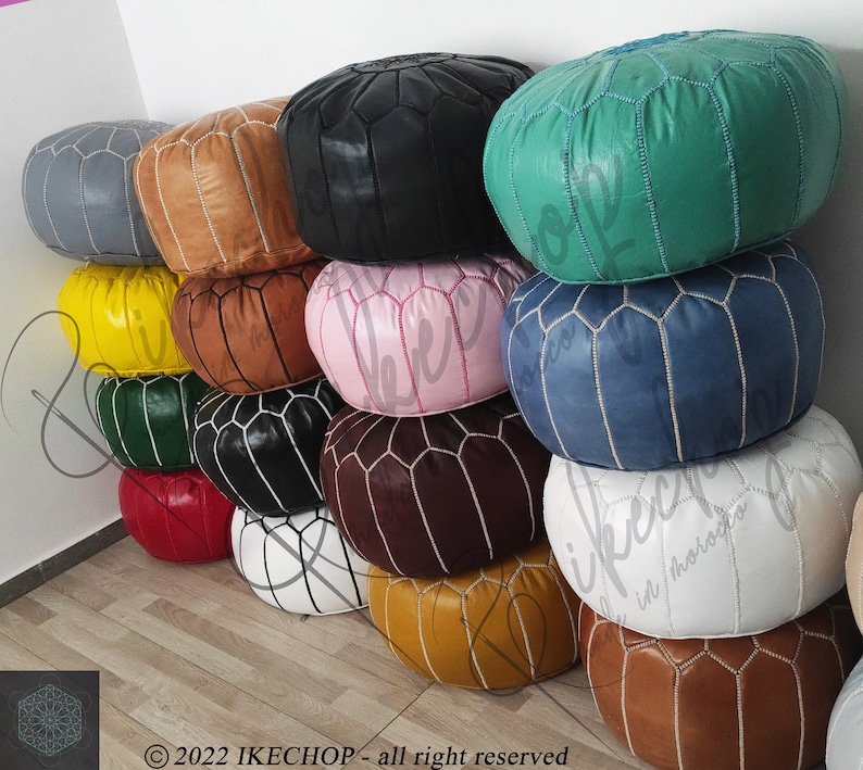 May include: A stack of colorful poufs made of leather with white stitching. The poufs are arranged in a pyramid shape, with the largest pouf at the bottom and the smallest pouf at the top. The poufs are in various colors, including yellow, green, blue, red, brown, black, and white.