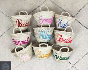 May include: Nine straw tote bags with personalized names in colorful embroidery. The names are:  "Alicia", "Sarah", "Kat", "Abby", "Christine", "Zoey", "Sammy", "Rebecca", and "Hannah".