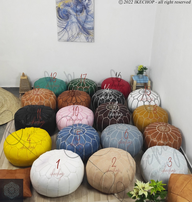 May include: A collection of 18 Moroccan poufs in various colors and patterns, including white, beige, yellow, blue, pink, brown, green, and red. The poufs are arranged in a circle on a white floor.