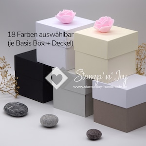 Könnte beinhalten: Fünf quadratische Geschenkboxen in verschiedenen Farben, darunter Weiß, Schwarz, Beige und Grau. Jede Box hat einen Deckel und ist mit einer kleinen rosa Blume verziert. Die Boxen sind pyramidenförmig auf einer weißen Oberfläche angeordnet. Der Text "18 Farben auswählbar (je Basis Box + Deckel)" ist im Bild sichtbar.