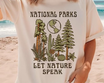 May include: Cream-colored t-shirt with the text "NATIONAL PARKS" above a graphic of trees, a globe, and plants. Below the graphic, the text reads "LET NATURE SPEAK". The shirt has short sleeves and a relaxed fit.