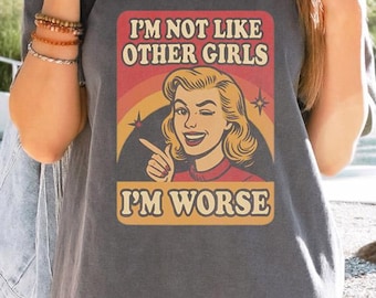 May include: Dark gray t-shirt with a retro graphic. The graphic features a winking woman with blonde hair, a red top, and the text "I'M NOT LIKE OTHER GIRLS I'M WORSE" in a vintage font.