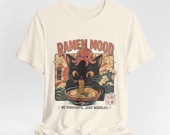 May include: A cream-colored t-shirt featuring a graphic of a black cat eating ramen with an octopus on its head. The text reads RAMEN MOOD and NO THOUGHTS, JUST NOODLES, accompanied by Japanese characters, a red sun, and blue waves in the background.