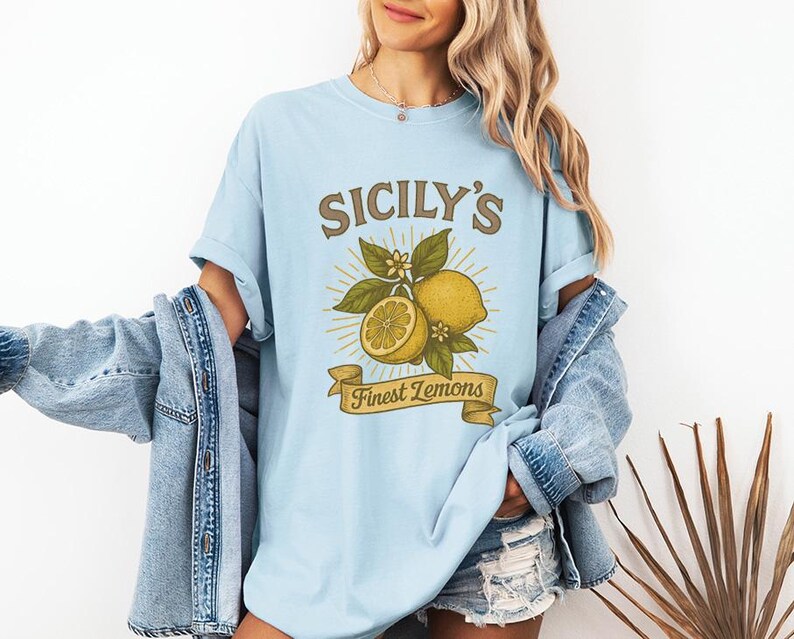 May include: Light blue t-shirt with the text "SICILY'S Finest Lemons" in a vintage style. The graphic features lemons, leaves, and flowers. The shirt is a soft, comfortable material.