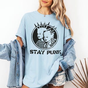 May include: A light blue t-shirt with a black and white graphic of two children with the text "Stay Punk".