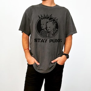May include: A gray t-shirt with a black graphic of two children with a mohawk and a bow. The graphic is inside a circle with the words "STAY PUNK" below it.