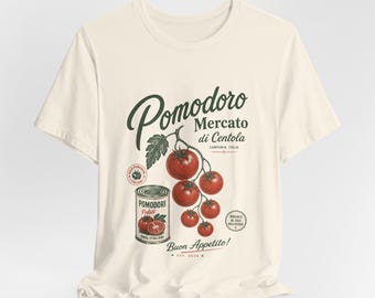 May include: A cream-colored t-shirt featuring a graphic of a vine of red tomatoes and a can labeled Pomodori Pelati. The text reads Pomodoro Mercato di Centola, Campania, Italia, Buon Appetito, and Est. 2024, with additional circular stamps.
