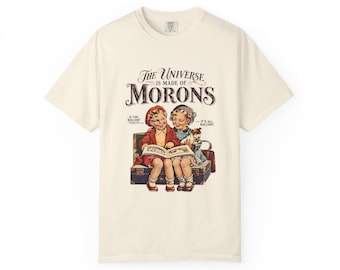 May include: An off-white short-sleeve t-shirt featuring a vintage-style illustration of two children reading a book. The text reads: The Universe is made of MORONS, Is this bullshit too???, and It's all bullshit. The graphic includes a suitcase.