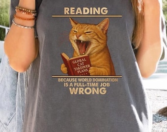 May include: Gray t-shirt featuring a cartoon cat reading a book titled "Global Cat Takeover Plans." The text above the cat reads "Reading," and below, "Because world domination is a full-time job wrong."