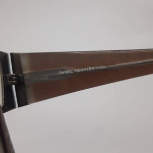 May include: Brown and black eyeglasses with a brown plastic frame and metal arms. The frame has the text "DANIEL HECHTER PARIS" printed on it.