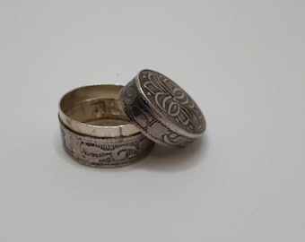 May include: A silver, round, decorative box with an intricate floral design. The box is open and the lid is sitting next to it.