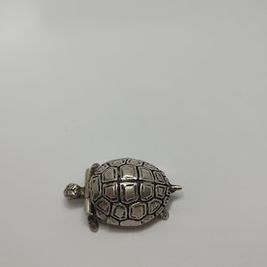 Pode incluir: Uma figura de tartaruga de prata com um design de concha detalhado.