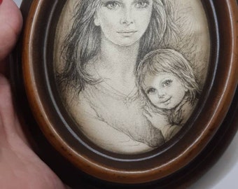 May include: A framed black and white pencil drawing of a woman and a child. The woman has long hair and is looking at the viewer. The child is looking to the side. The frame is oval shaped and made of dark wood.