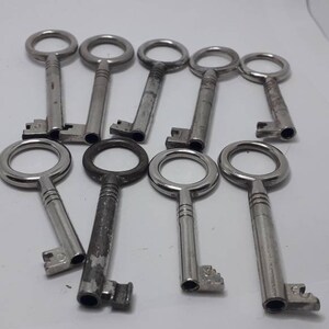 May include: A collection of ten silver-toned keys with round keyholes. The keys are arranged in a semi-circle on a white surface.