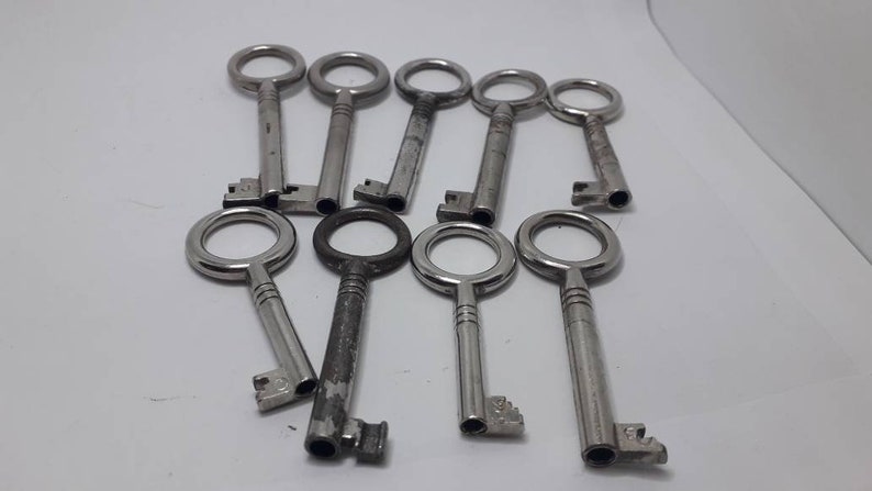 May include: A collection of ten silver-toned keys with round keyholes. The keys are arranged in a semi-circle on a white surface.