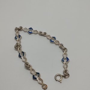 May include: A silver bracelet with a blue enamel design. The bracelet is made of a chain of linked diamond shapes with blue enamel in the center of each diamond.