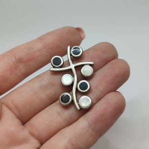 Può includere: Un ciondolo d'argento con un designo a ramo stilizzato con pietre rotonde bianche e nere.