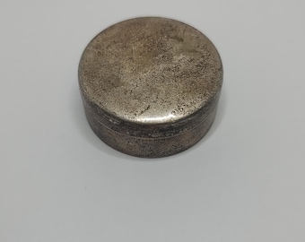 May include: A round, silver trinket box with a slightly worn surface.