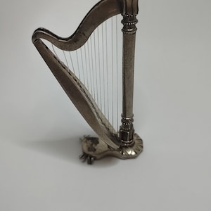 Op de afbeelding: Een zilveren miniatuurharp met een gedetailleerd ontwerp en snaren. De harp staat op een wit oppervlak.