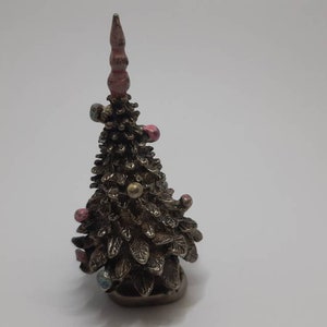 Puede incluir: Un pequeño adorno de árbol de Navidad de color dorado con una estrella rosa en la parte superior y adornos coloridos que cuelgan de las ramas.