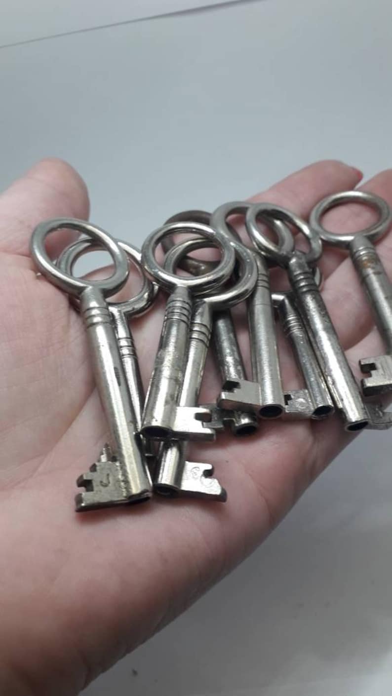 May include: A collection of vintage silver keys with intricate designs and different sized keyholes. The keys are held in a hand.
