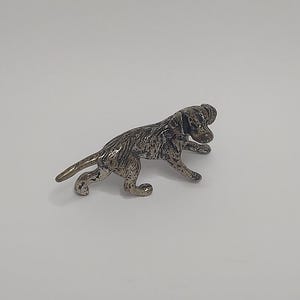 May include: A silver-colored metal figurine of a dog in a running pose. The dog is detailed with textured fur and has a slightly raised head.