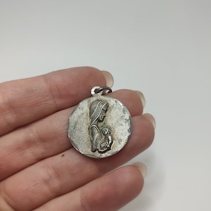 May include: Silver pendant featuring a relief of the Virgin Mary holding a baby Jesus.