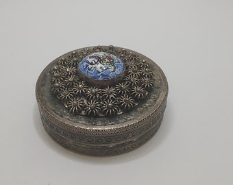 May include: A silver round trinket box with a floral design around the lid. The lid has a blue and white enamel center with a floral design.