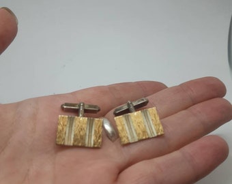 Puede incluir: Un par de gemelos de oro y plata con un diseño texturizado. Los gemelos son de forma cuadrada y tienen una parte posterior plateada.