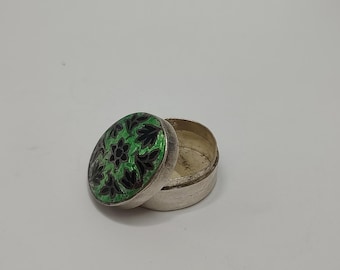 May include: A small, round, silver trinket box with a green and black enamel lid. The lid features a floral design.