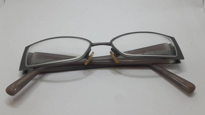 May include: A pair of gray metal eyeglasses with a rectangular frame and brown arms.