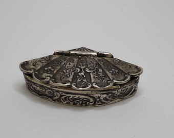 Könnte beinhalten: Eine silberne, verzierte, Scharnier-Box in Form einer Muschel. Die Box ist mit komplizierten floralen Designs verziert.
