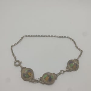 May include: Silver-toned bracelet featuring three circular, decorative elements with colorful enamel designs. The bracelet has a delicate chain and a clasp closure. The enamel colors include yellow, green, and purple.