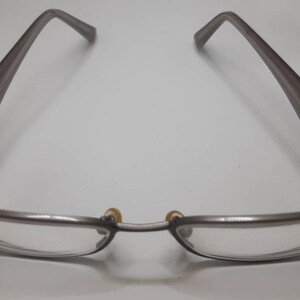 May include: A pair of silver-toned eyeglasses with a rectangular frame and clear lenses. The arms of the glasses are a darker shade of gray.