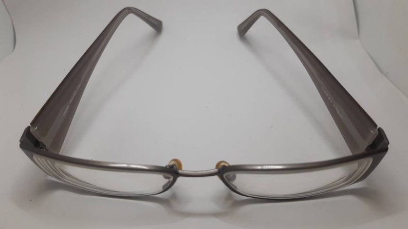 May include: A pair of silver-toned eyeglasses with a rectangular frame and clear lenses. The arms of the glasses are a darker shade of gray.