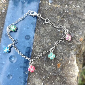 May include: A silver charm bracelet with five charms in the shape of four-leaf clovers. The charms are decorated with enamel in shades of pink, blue, and green.