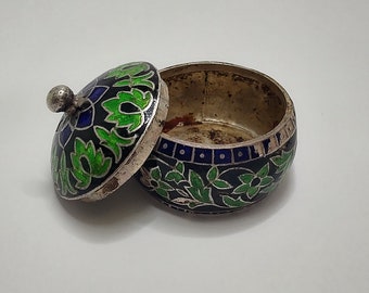 May include: A small, round, silver trinket box with a lid. The box is decorated with green and blue enamel floral designs on a black background.