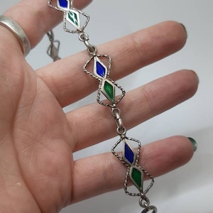 Puede incluir: Un brazalete de plata con un diseño de cadena de eslabones y formas de diamante de esmalte azul y verde alternadas. El brazalete tiene un cierre de langosta.