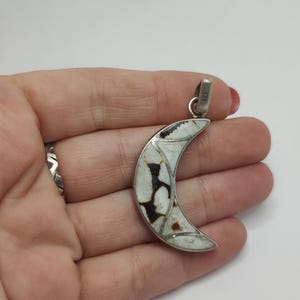 Peut inclure: Pendentif en forme de croissant de lune avec un cadre en métal argenté. Le pendentif présente un motif en mosaïque blanc et marron. La bélière est marquée "925". Un bijou unique.