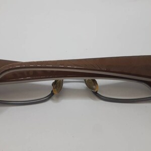 May include: Brown and silver eyeglasses with a brown leather frame. The frame has a textured pattern.