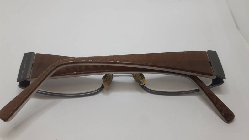 May include: Brown and silver eyeglasses with a brown leather frame. The frame has a textured pattern.