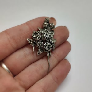 以下が含まれることがあります： 葉のついた、詳細なバラの花の房が特徴の銀製のブローチ。ブローチはピン留めです。