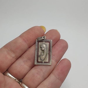 May include: Silver pendant featuring a rectangular frame with a detailed design. Inside the frame is a depiction of the Virgin Mary in profile, with her hands clasped in prayer.