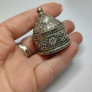 May include: A silver trinket box with an ornate floral design. The box has a domed lid and a round base.