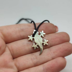 Può includere: Una collana con un ciondolo a forma di lucertola argentata e un cordoncino nero. Il ciondolo ha il nome "Berenice" inciso.